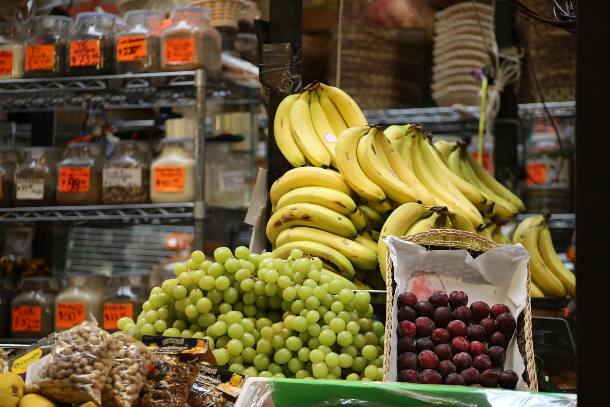 A vibrant assortment of bananas, grapes, and plums at a bustling market stand.