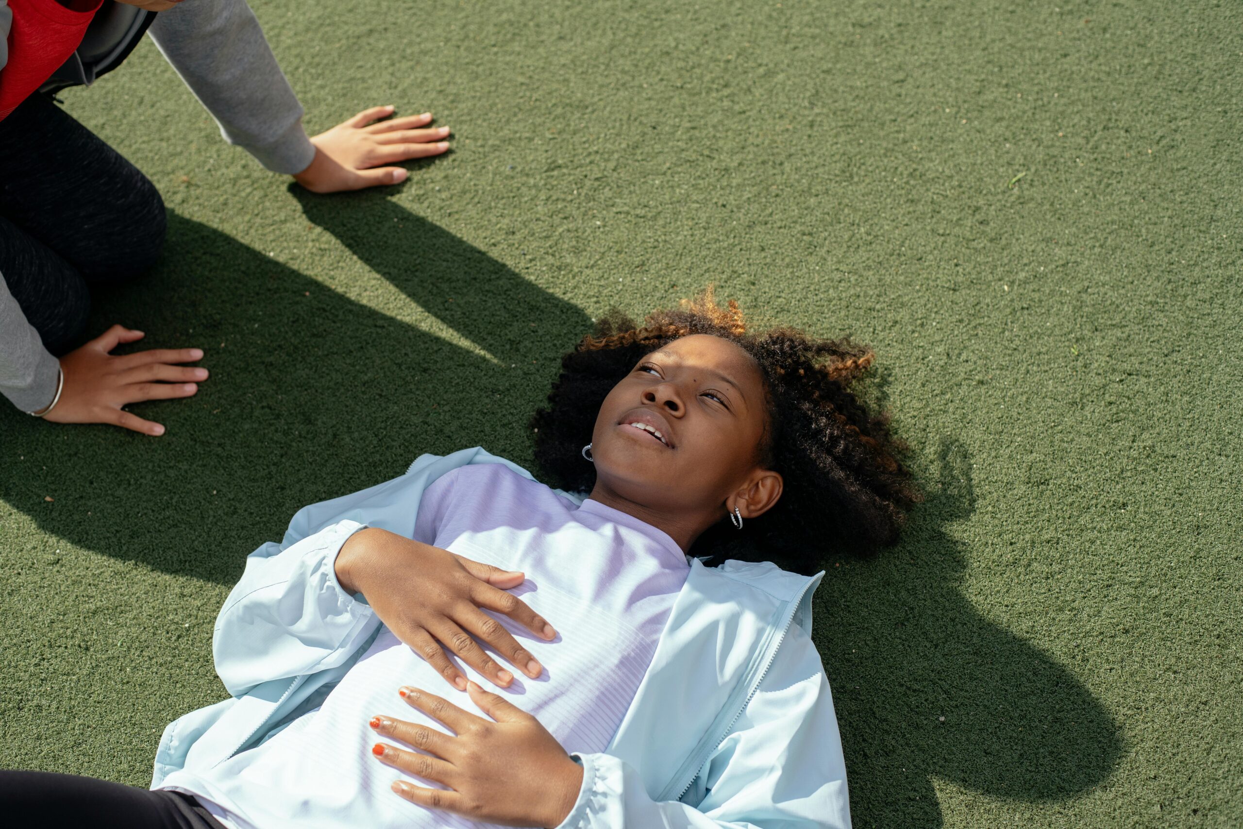 High angle of African American girl in casual clothes relaxing on sports ground in shade of unrecognizable friend