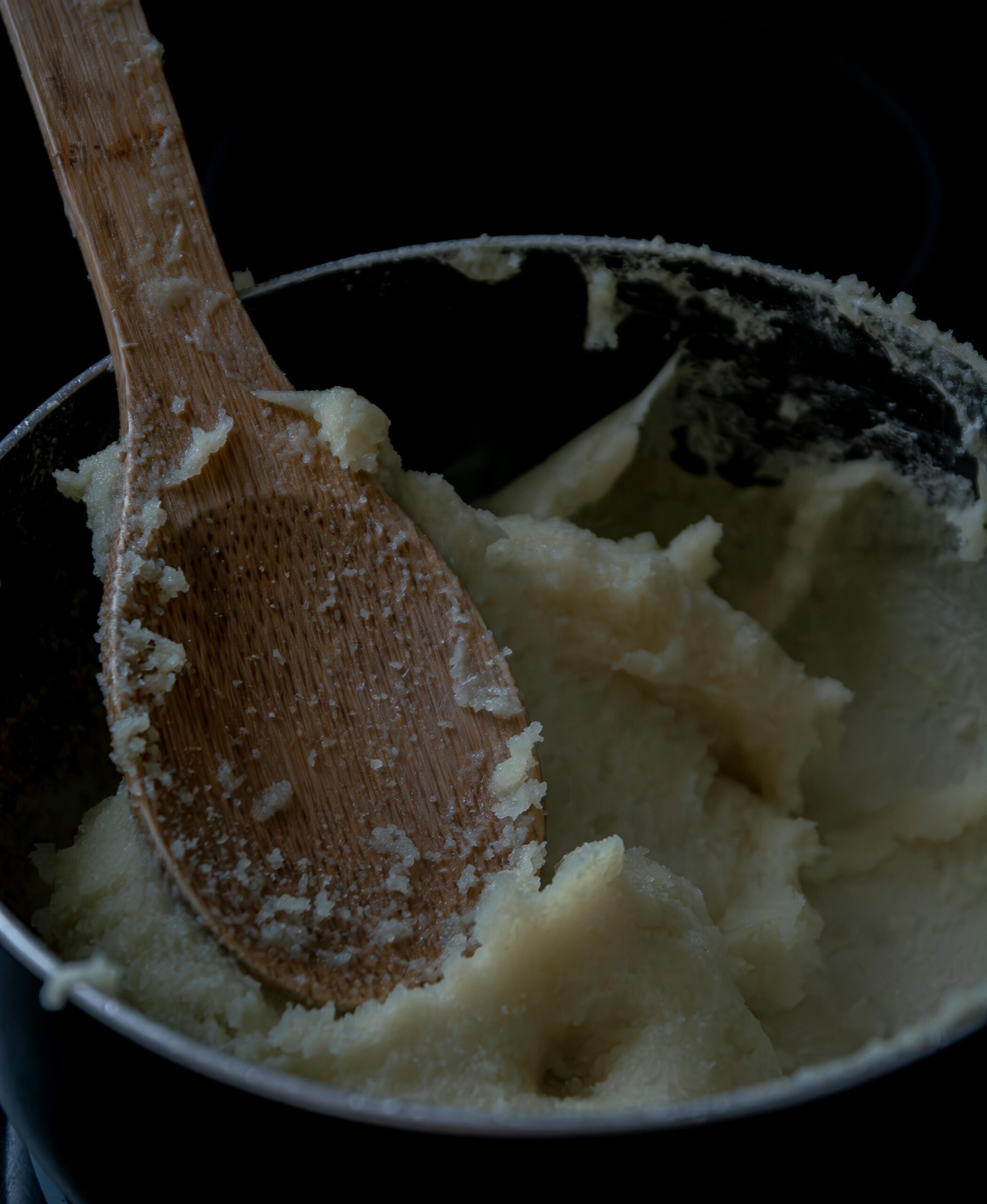 A close-up of creamy mashed potatoes in a pot with a wooden spoon, perfect for food enthusiasts.
